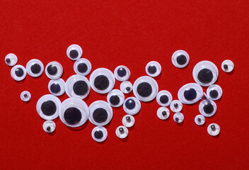 Various sizes of kids art fun googly eyes on red background. Top view