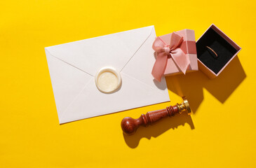 Wedding proposal. Envelope with vintage stamp and gift box with gold ring on yellow background