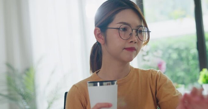 Young Asia female freelance eyeglasses drink coffee and type write prompt AI bot IT app program nomad, video game, terminal with coding, user interface, data center on desktop computer at home office.