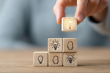 Hand building idea pyramid with lightbulb and head symbols on wooden blocks