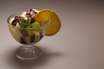 A delightful glass bowl of creamy ice cream, topped with chocolate syrup, assorted fruit, and whipped cream