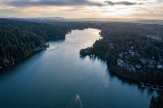 Aerial drone picture of Lake Oswego, Oregon, showing calm blue water surrounded by dense forest and residential houses, real estate, on a clear sunny evening at sunset. Captured at early fall.