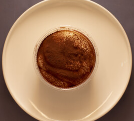 A delightful cup of rich tiramisu dessert is artfully arranged on a pristine white plate against a dark background