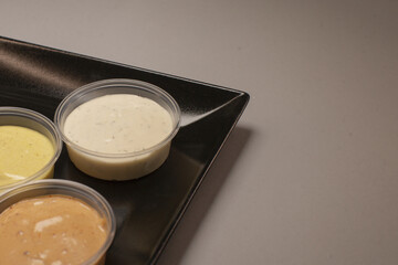 Three elegant saucefilled containers are artfully arranged on a sleek black plate, against a soft grey background