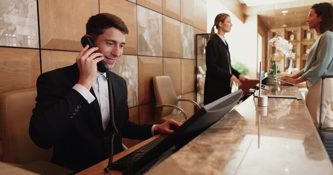 Male hotel receptionist sits at front desk, speaks on phone