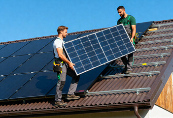professional workers installing photovoltaic solar panels on a metal rooftop under clear skies. 