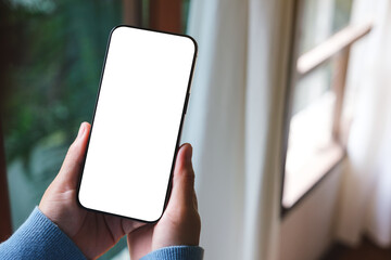 Mockup image of a woman holding mobile phone with blank desktop screen at home