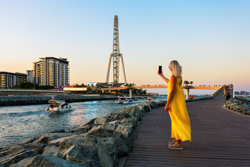 Mature woman tourist in yellow dress in Dubai marina taking selfie.
