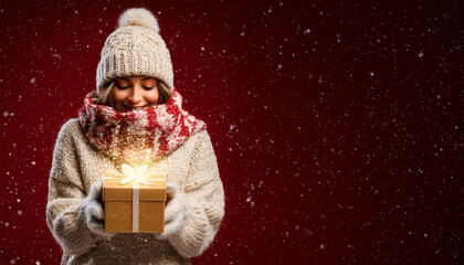 Portrait of happy smiling young woman holding festive red gift box in her hands on Christmas tree background in winter forest, wearing white hat, jacket outdoors