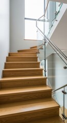 Modern residential interior featuring a stylish wooden staircase with a sleek glass balustrade and stainless steel handrail, illuminated by natural light from a large window.
