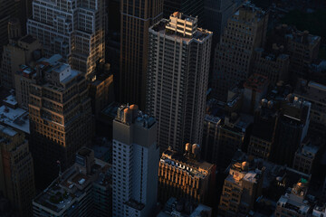 View of Manhattan high-rises in evening light. Tall buildings, rooftop water towers, and deep shadows create a striking urban cityscape in New York City. © PW PRO MEDIA