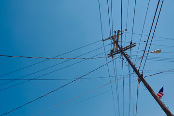 Utility pole with power lines crossing the sky, photographed against a clear blue background. An American flag is visible in the corner, adding context to the urban scene.