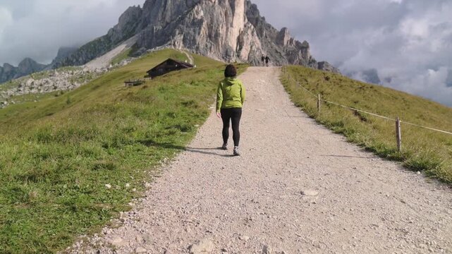 Backpacker on alpine trail with mountain hut and iconic formation ahead Solo hiker walking toward rocky towers of Cinque Torri in the Dolomitines Alpes