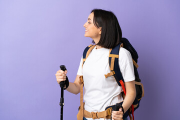 Young caucasian woman with backpack and trekking poles isolated on blue background laughing in...
