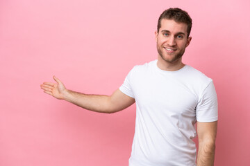 Young caucasian man isolated on pink background extending hands to the side for inviting to come