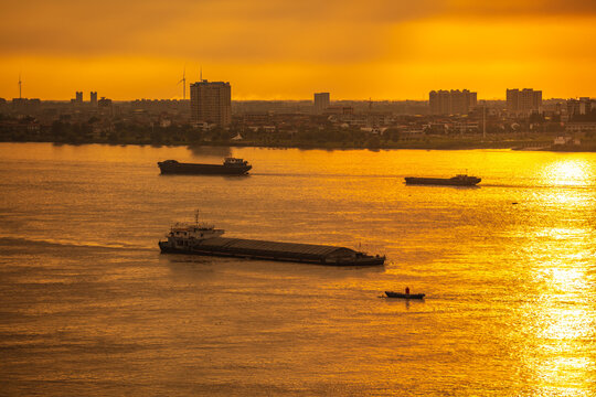 The Yangtze River and its shipping vessels, bathed in the glow of the setting sun, are located in Jiujiang, a historical and cultural ancient city in eastern Asia, Jiangxi Province, China.