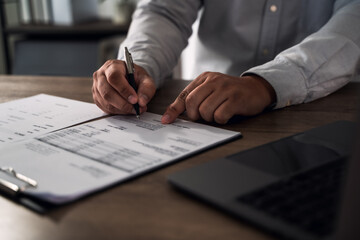 Contract signing concept for finance approval: close-up of hands reviewing and signing paperwork on...