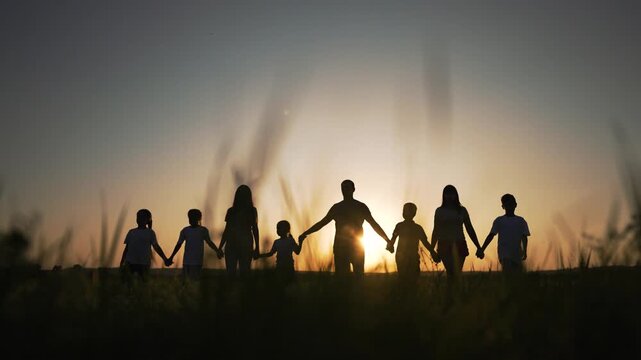 Holding hands across golden sunset field silhouette of family parent and child walk in unity in tall grass holding hand with sun setting behind horizon creating warm outline and linked silhouette