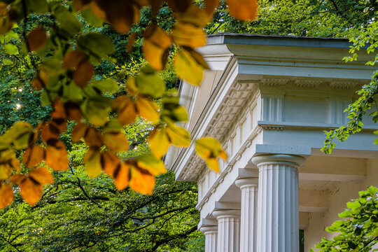 A classic pavilion with white columns in a green park, framed by autumn-colored foliage, illuminated by warm sunlight