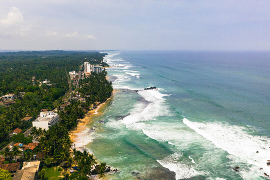 Drone view of tropical beach in Sri Lanka with ocean waves, palm trees, and golden sand coastline.