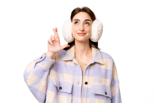Young caucasian woman wearing winter muffs over isolated chroma key background with fingers crossing and wishing the best