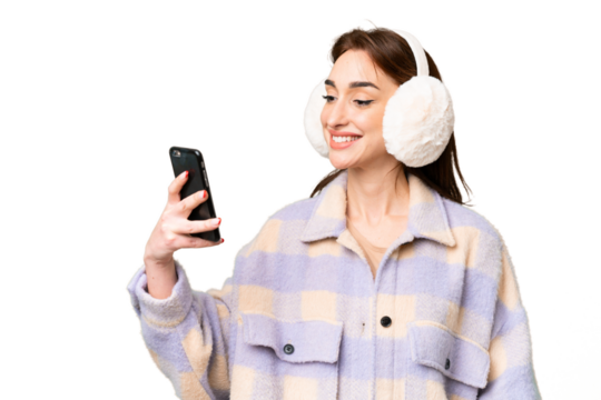 Young caucasian woman wearing winter muffs over isolated chroma key background making a selfie - Powered by Adobe