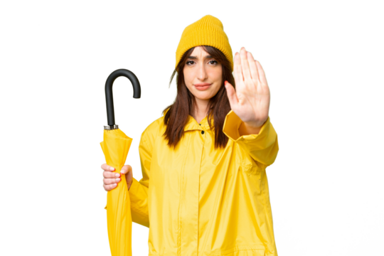 Young caucasian woman with rainproof coat and umbrella over isolated chroma key background making stop gesture - Powered by Adobe