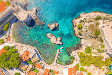 Drone top down image of Sulic Beach in Dubrovnik showing turquoise Adriatic waters, and medieval city walls and scenic coastal summer atmosphere in Croatia
