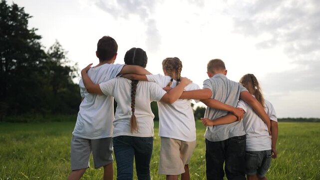 Children hug in grassy field together while group of kids link arms in warm summer light showing friendship and joy in outdoor nature play with child connection and shared laughter and carefree bond