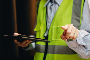 Professional worker in safety vest pointing with tablet in hand, emphasizing importance of safety and communication in workplace