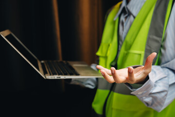 Worker in Safety Vest Using Laptop with One Hand While Displaying Open Hand in a Modern Workspace Environment
