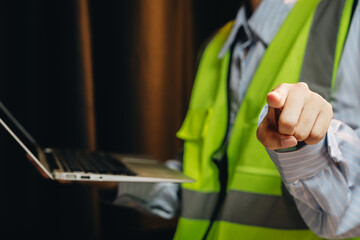 Construction worker in safety vest pointing with laptop during safety meeting or training session indoors