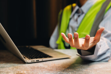 Professional construction worker in reflective vest gestures while consulting a laptop during a project meeting indoors