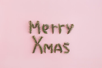 Quote Merry Xmas made of fir tree branches on pink background. Minimal Christmas postcard, banner