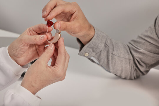 Man patient with hearing problem receives ready-made BTE hearing aids with individual inserts from audiologist, close-up