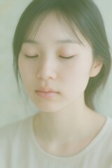 Serene portrait of a young woman with closed eyes in a soft, ethereal light.