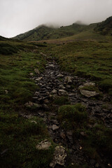 Close-up of rocks on mountain slope, green meadow and low clouds over hills