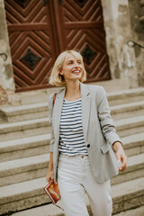 Woman in a blazer walks down steps with a smile in a charming old town setting