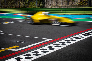 Bliurred motion of yellow car crossing finish line sign on asphalt track