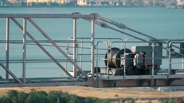 close-up view of the moving parts of a tower crane against the backdrop of a sea, ocean, or river. The crane hoist mechanism and cable are rotating.