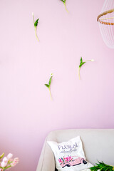 Floral decorative elements arranged on a pastel pink wall, with a cozy couch and a stylish pillow, creating a serene and inviting interior design atmosphere