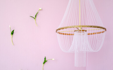 Elegant chandelier with delicate beadwork hangs from ceiling against soft pink wall, surrounded by minimalistic floral accents, creating a serene and stylish atmosphere. Copy space