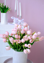 Pink tulips arranged in a white vase on a minimalist table, surrounded by elegant candles and greenery, creating a serene and inviting atmosphere for home decor