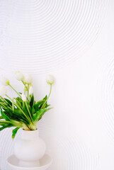 White vase filled with fresh tulips sits against a textured white wall, creating a serene and elegant atmosphere, perfect for home decor or floral arrangements. Copy space