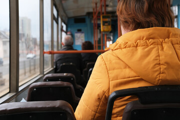 Woman wearing a yellow jacket is seated on a public transport bus, with passengers in the background, showcasing urban commuting and everyday life experience