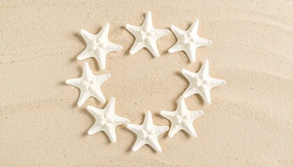 Nine white starfish form a perfect ring around one beige center on soft sand.