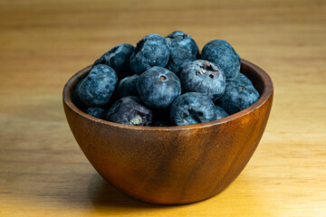 Closeup view of ripe sweet blueberry fruits in wooden bowl on wooden table.