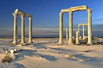 Fototapeta premium Ruined columns stand under a clear blue sky on sandy land
