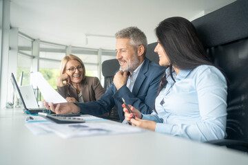 Three busy happy middle aged professional business man and two women executive leaders team using laptop working on computer at work desk having conversation on financial project at meeting in office.