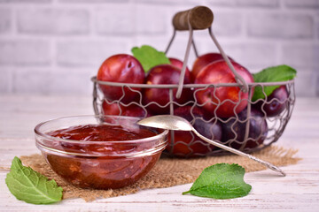 Homemade plum jam in a glass bowl against the background of a basket of plums. Plum jam.
